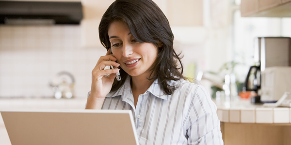 woman speaking on the phone while using a laptop